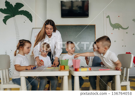 Holding markers, learning to draw. Children in kindergarten with their teacher Holding markers, learning to draw. Children in kindergarten with their teacher 136764058