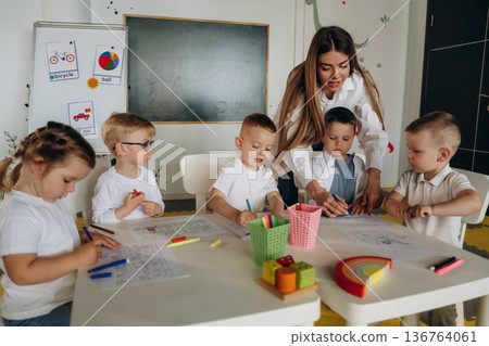 Holding markers, learning to draw. Children in kindergarten with their teacher 136764061
