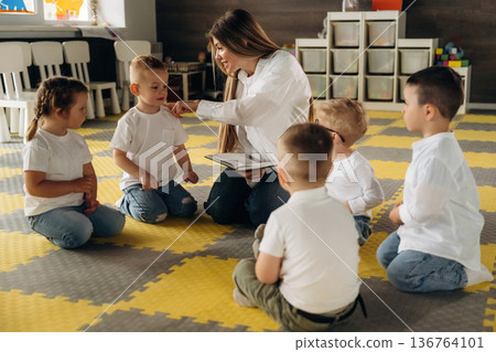 With book, sitting on the floor. Children in kindergarten with their teacher With book, sitting on the floor. Children in kindergarten with their teacher 136764101