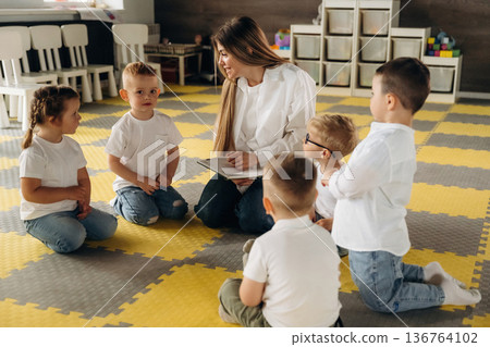 With book, sitting on the floor. Children in kindergarten with their teacher With book, sitting on the floor. Children in kindergarten with their teacher 136764102