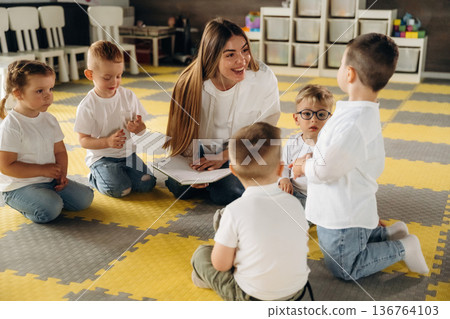 On the floor, learning new words. Children in kindergarten with their teacher On the floor, learning new words. Children in kindergarten with their teacher 136764103