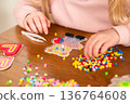Child's hands creating a bear pattern with colorful fuse beads on a wooden table. Creative DIY craft at home. Thermo mosaic, ironing beads, fuse beads 136764608