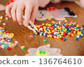 Child hand sorting thermomosaic ironing beads fuse beads on wooden table close up 136764610