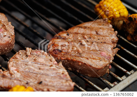 Juicy steaks and grilled corn cooking on a warm summer evening barbecue party Juicy steaks and grilled corn cooking on a warm summer evening barbecue party 136765002