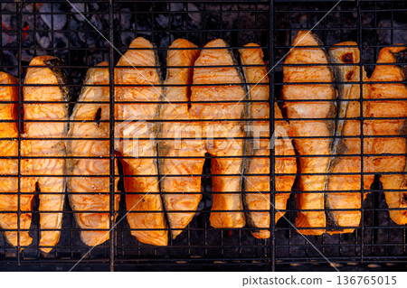 Fresh salmon fillets grilling over charcoal at a summer outdoor barbecue party Fresh salmon fillets grilling over charcoal at a summer outdoor barbecue party 136765015