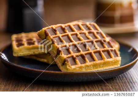 Sweet waffles with chocolate on plate on wooden table. 136765087