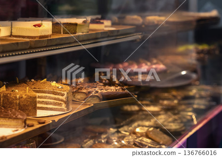 Bakery display case with cake slices, pastry and chocolate dessert arranged on shelves behind glass. Bakery showcase, dessert selection, confectionery retail business 136766016