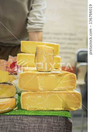 Cheese blocks stacked on market counter in dairy shop setting. Concept of local food market sale, dairy product assortment, farm food retail 136766019