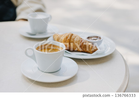Cup of black coffee and a croissant on a table in a street cafe. Cup of black coffee and a croissant on a table in a street cafe. 136766333