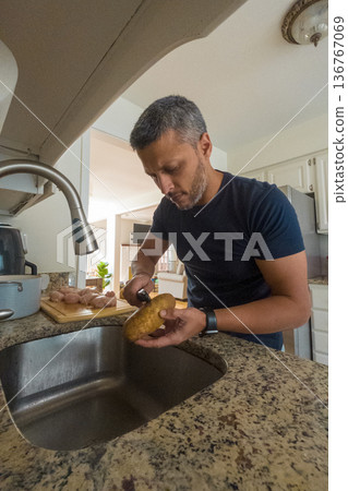 A man is cutting a potato in a kitchen sink A man is cutting a potato in a kitchen sink 136767069