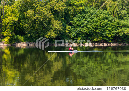 A man in a red boat is rowing across a lake A man in a red boat is rowing across a lake 136767088