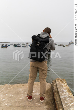 A man with a backpack is taking a picture of the ocean A man with a backpack is taking a picture of the ocean 136767101
