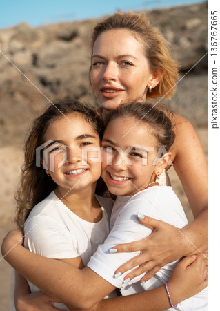 Loving mother embracing daughters on sandy beach Loving mother embracing daughters on sandy beach 136767665