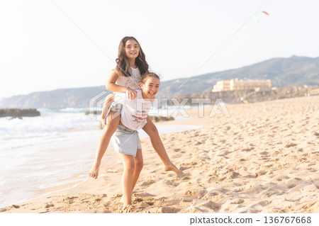 Cheerful girls playing piggyback ride on sandy 136767668