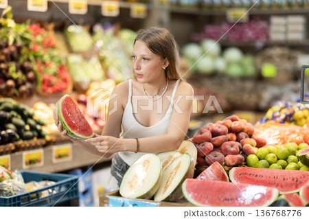Girl choosing ripe tasty watermelon in grocery department of supermarket 136768776