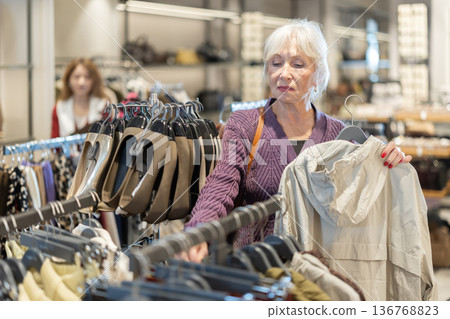 Attentive mature woman choosing outerwear in clothing store 136768823