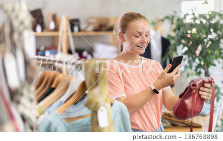 Teenage girl scans qr code of handbag in clothing store Teenage girl scans qr code of handbag in clothing store 136768898