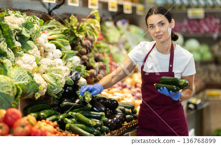 Girl seller puts ripe zucchini in pods in box on display case 136768899