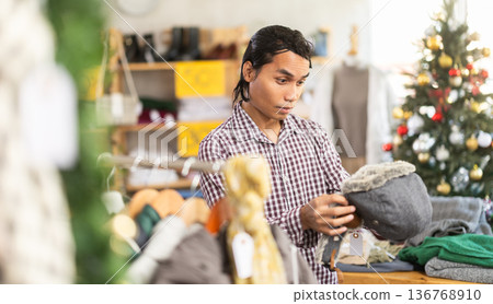 In chain shop, amazed Indonesian man choose hat cap with earflaps In chain shop, amazed Indonesian man choose hat cap with earflaps 136768910
