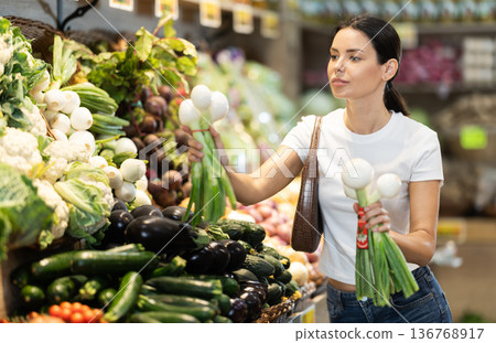 woman chooses a large onion with green stems 136768917