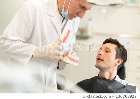 Elderly male dentist showing model of teeth to patient 136768922