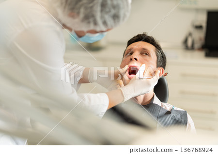 Girl doctor dentist in white coat examines oral cavity of man patient in dentistry. 136768924