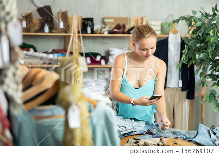 Teenage girl scanning QR-code on pantaloons in clothing store Teenage girl scanning QR-code on pantaloons in clothing store 136769107
