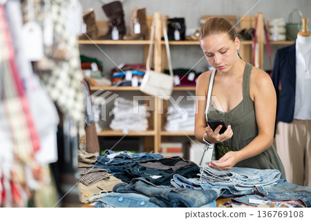 Teenage girl scanning QR-code on pantaloons in clothing store Teenage girl scanning QR-code on pantaloons in clothing store 136769108