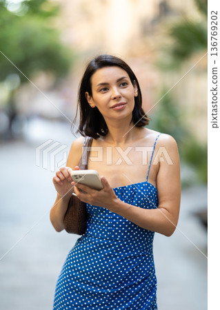 Happy young girl with mobile phone in her hands walking around city and taking pictures of sights 136769202