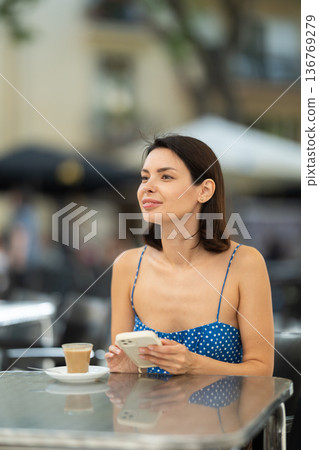 Young woman with phone drinking coffee in cafe 136769279