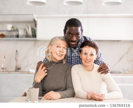 Middle-aged man and two women posing at the kitchen-table 136769319