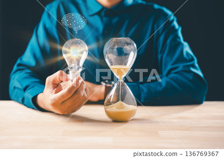 Glowing lightbulb, hourglass, sand, time concept for new idea, business innovation and deadline countdown, for creative thinking and solution Glowing lightbulb, hourglass, sand, time concept for new idea, business innovation and deadline countdown, for creative thinking and solution 136769367