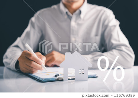 Considering a mortgage for your next home, this image shows a man analyzing paperwork with a house figure, investment and the percent symbol, illustrating real estate business and another mortgage Considering a mortgage for your next home, this image shows a man analyzing paperwork with a house figure, investment and the percent symbol, illustrating real estate business and another mortgage 136769389