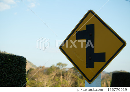 Yellow winding road warning sign indicating multiple curves ahead on a rural mountain route under clear daylight sky. 136770919