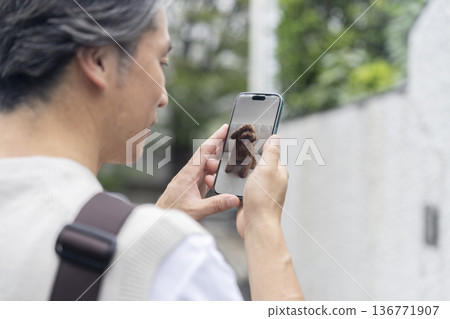 畫面中,一位中年男子獨自在家,透過智慧型手機上的寵物攝影機查看他的寵物狗的狀況。 畫面中,一位中年男子獨自在家,透過智慧型手機上的寵物攝影機查看他的寵物狗的狀況。 136771907