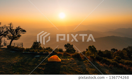 Beautiful morning sunrise over mountain layers with a yellow camping tent and a relaxing traveler. Beautiful morning sunrise over mountain layers with a yellow camping tent and a relaxing traveler. 136774268