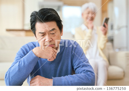 Worried Asian senior man and his carefree wife Worried Asian senior man and his carefree wife 136775250