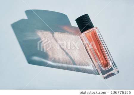 Perfume bottle on light blue surface creating sunlit shadow and light patterns 136776196