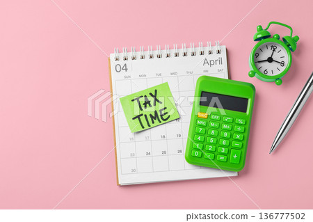 Tax time word on green sticky note on calendar with clock and calculator on pink background, financial and accounting planning, tax season, top view 136777502