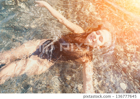 Woman floating water young lady in black swimsuit relaxes in clear sea with rocky bottom under bright golden sunlight Woman floating water young lady in black swimsuit relaxes in clear sea with rocky bottom under bright golden sunlight 136777645