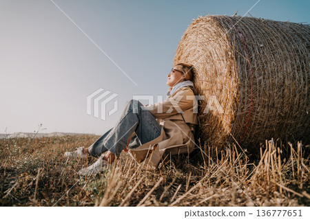 Woman Relaxing by a Hay Bale in a Field 136777651