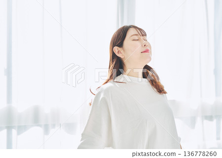 A woman taking a deep breath and relaxing in natural morning light A woman taking a deep breath and relaxing in natural morning light 136778260