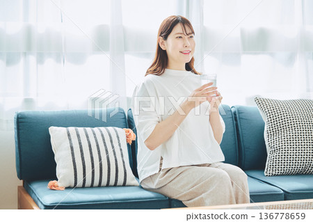 A healthy woman hydrating in her living room at home 136778659