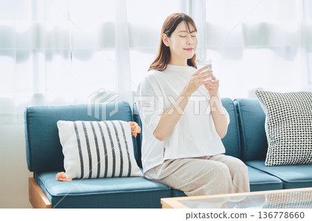 A healthy woman hydrating in her living room at home 136778660