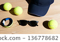 Tennis essentials: cap, sunglasses, wristband, tennis balls on wooden surface 136778682