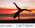 Silhouette of young female performing cartwheel on sunset beach 136778693