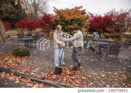 Father and teenage daughter placing no parking sign while closing outdoor cafe terrace at end of autumn season 136778931