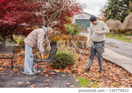 Father and teenage daughter cleaning fallen autumn leaves at outdoor cafe terrace closing seasonal small business 136778932