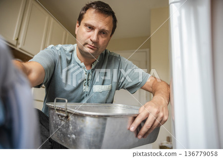 Middle aged man loading laundry into washing machine at home doing household chores and managing everyday domestic routine 136779058