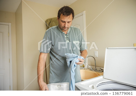 Middle aged man sorting clothes before washing at home preparing laundry for washing machine during daily household routine Middle aged man sorting clothes before washing at home preparing laundry for washing machine during daily household routine 136779061